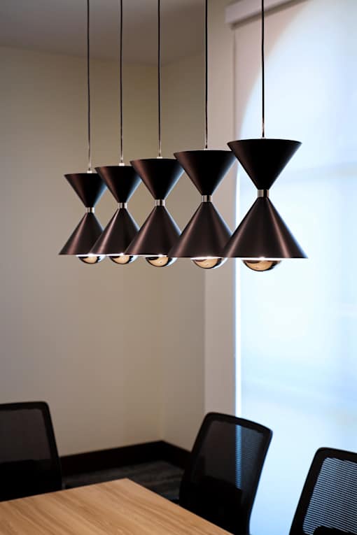 A group of black hanging lamps with a wooden table and chairs below.
