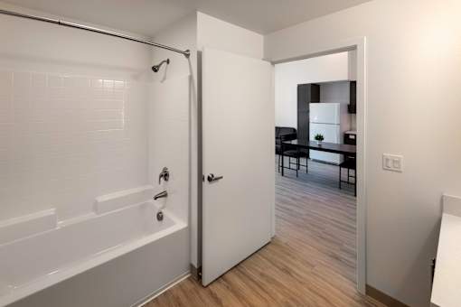 A white bathroom with a tub and a door leading to a living room.
