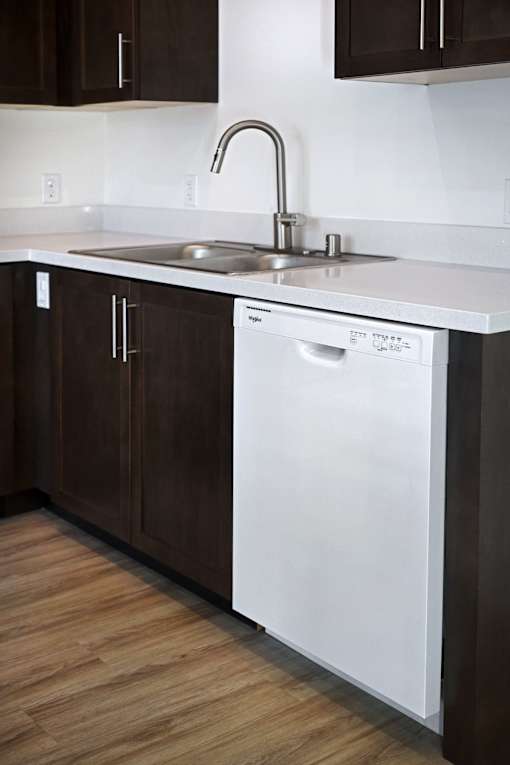 A white dishwasher is in a kitchen with dark brown cabinets.