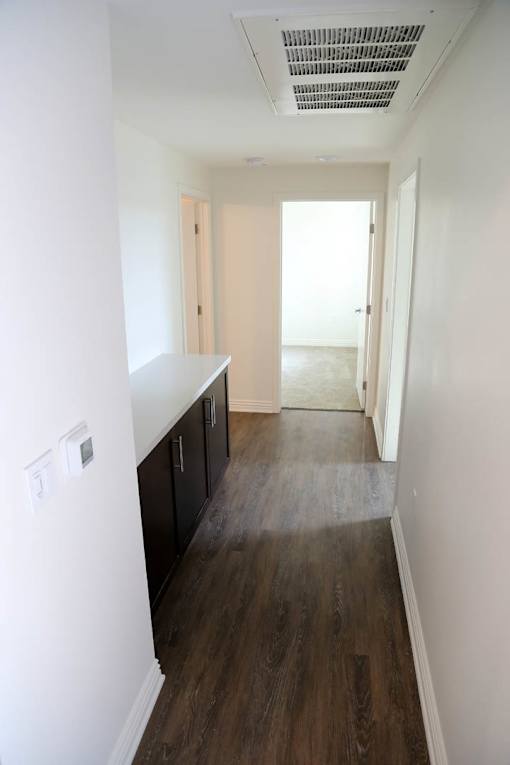 A long, narrow hallway with dark wood floors and white walls.