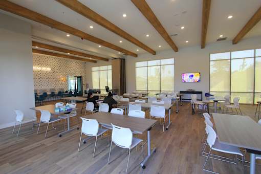 A conference room with a long table and chairs, a television on the wall, and a view of the outdoors through the windows.