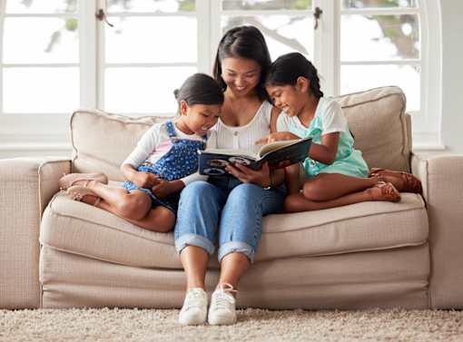 A woman and two children are sitting on a couch reading a book together.