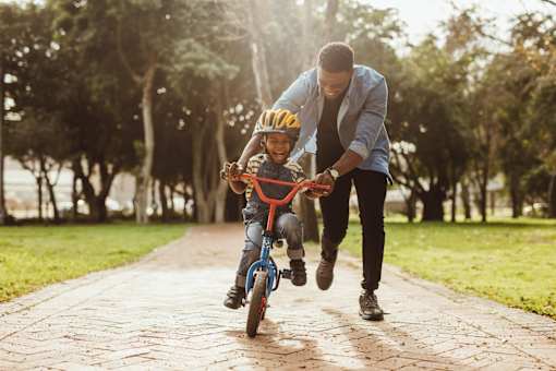 A man is helping a child ride a bicycle in a park.