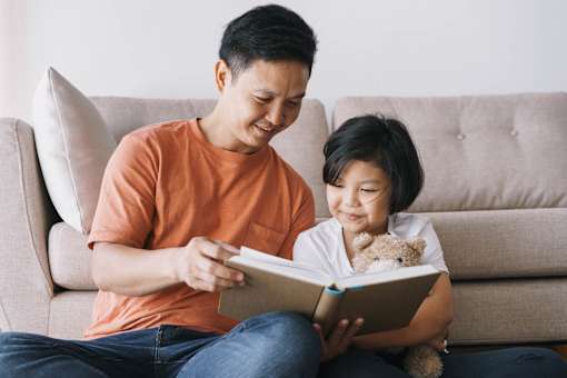 A man and a child are reading a book together on a couch.