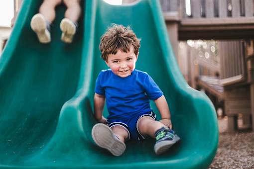 A young boy in a blue shirt and shorts is sitting on a green slide.