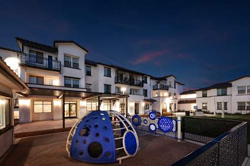 A playground area with a slide and a ball pit in front of apartment buildings at dusk.
