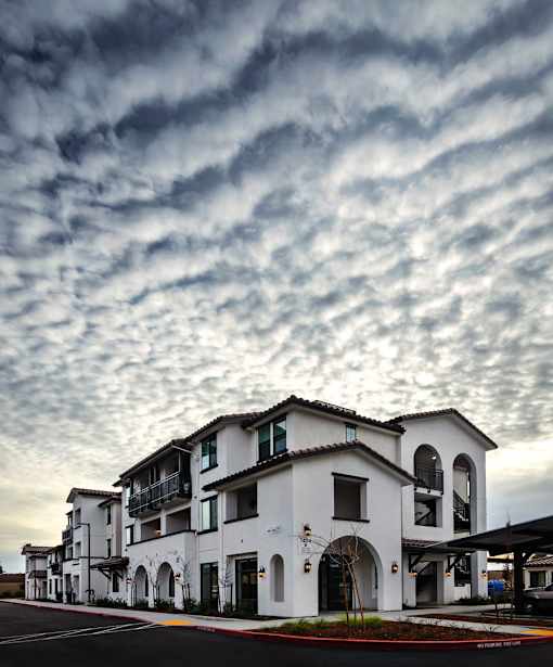 A row of white buildings with balconies and arches are under a cloudy sky.