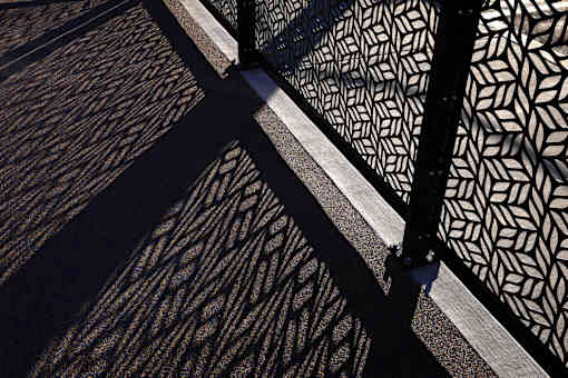 A black and white patterned fence casts a shadow on the ground.