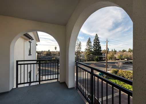 A balcony with a black railing and a view of a parking lot and trees.