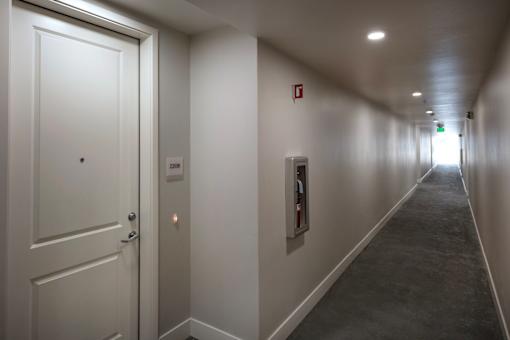 A long hallway with a door on the left and a fire extinguisher on the wall on the right.