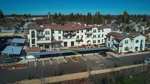 A large white building with a red roof is surrounded by a parking lot.