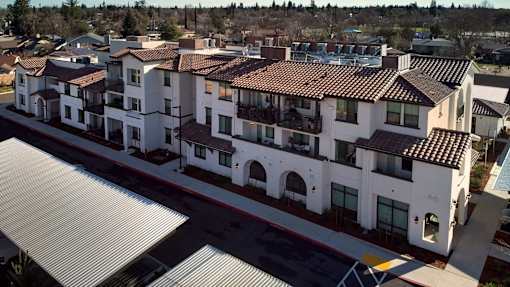 A large white building with a red tile roof is surrounded by a parking lot.