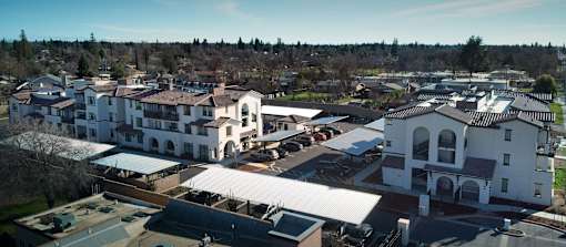 A large white building with a red roof is surrounded by other buildings.