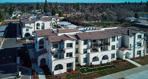 A large white building with a red roof is surrounded by smaller buildings.