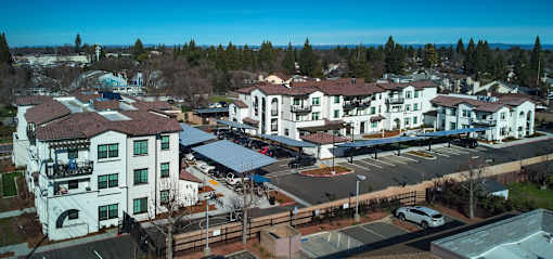A large white building with a red roof is surrounded by a parking lot.