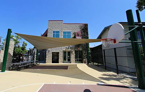 A basketball court is located in front of a building with a basketball hoop on the right side.