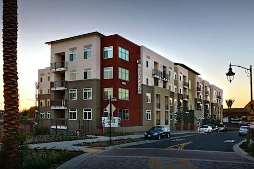 A street view of a residential area with apartment buildings and cars parked on the side of the road.