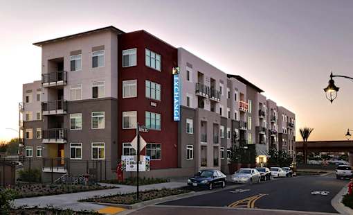 A street view of apartment buildings with cars parked on the side of the road.