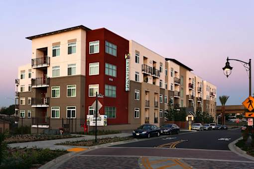 Apartment buildings line a street with cars parked on the side.