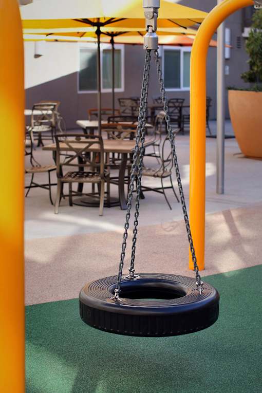 A swing set with a yellow pole and a black seat.