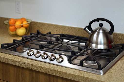 A silver kettle is on a stove with six burners.