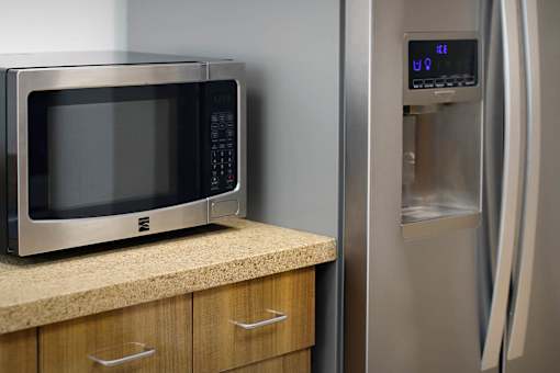 A microwave is on a countertop next to a stainless steel refrigerator.