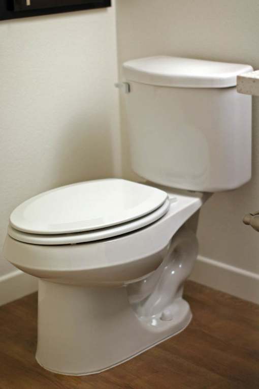 A white toilet with a white lid and tank sits on a wooden floor.