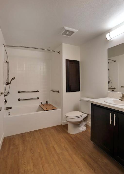 A bathroom with a white toilet, a white sink, and a white bathtub with a wooden mat.