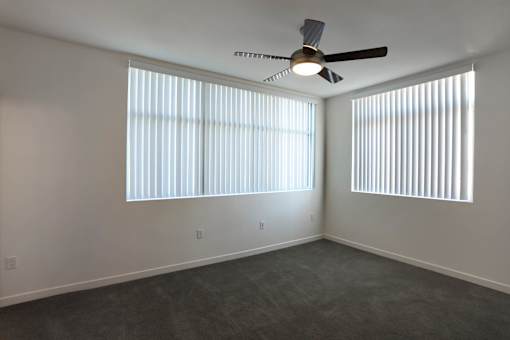 A room with a ceiling fan and two windows with blinds.