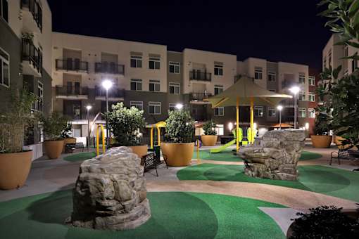 A playground area with a green surface and a large rock in the middle.