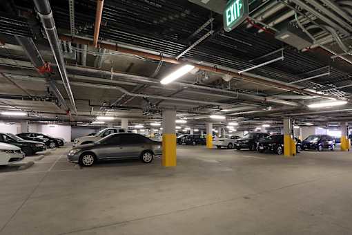 A parking garage with a green exit sign and cars parked in it.