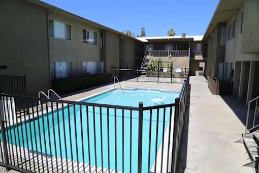 A black fence surrounds a blue pool in a residential area.