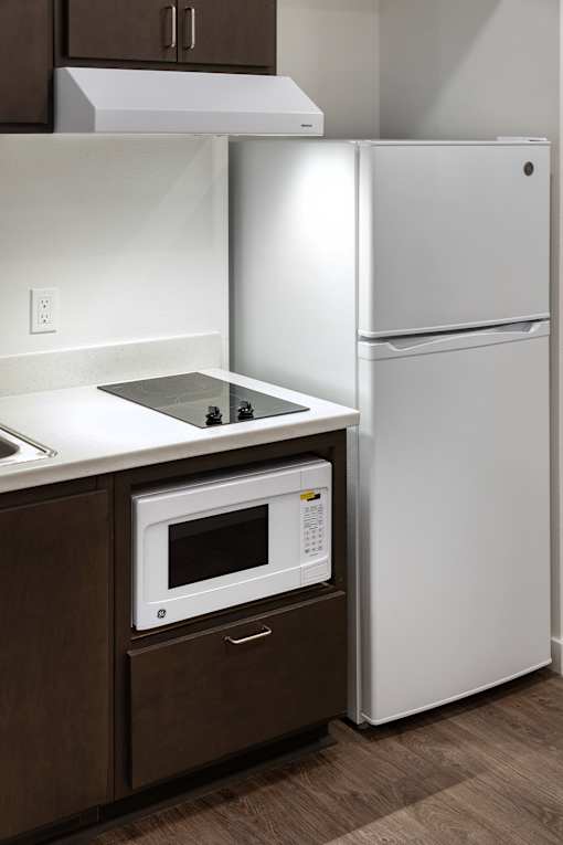 A white refrigerator stands next to a microwave in a kitchen.