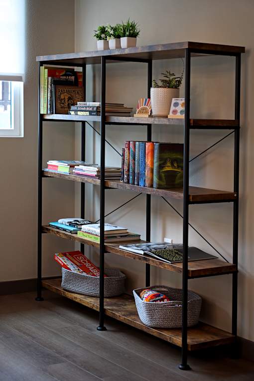 A black shelving unit with books, plants, and baskets on it.