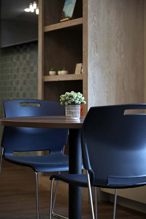 Two blue chairs are placed in front of a wooden table with a vase of flowers on it.
