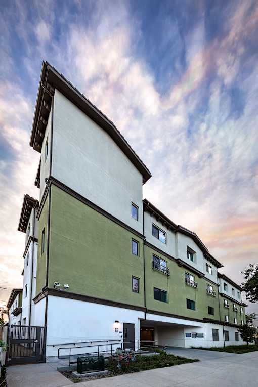 A building with a white and green facade is shown with a cloudy sky in the background.