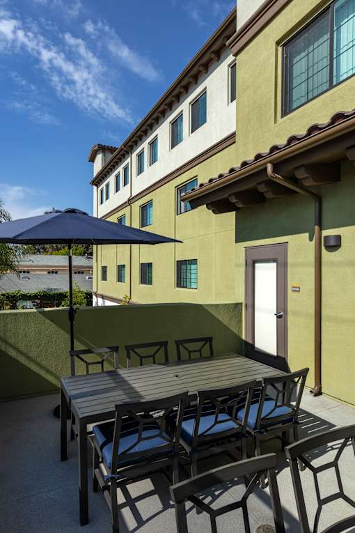 A patio with a table and chairs and a blue umbrella.