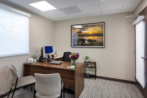 A room with a desk, chair, and a painting on the wall.