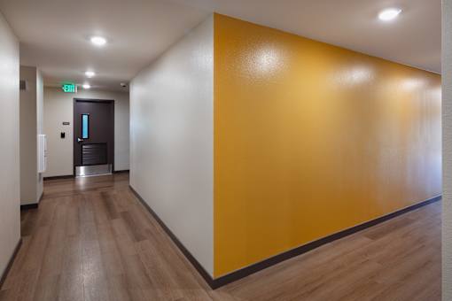 A hallway with a wooden floor and a yellow wall.