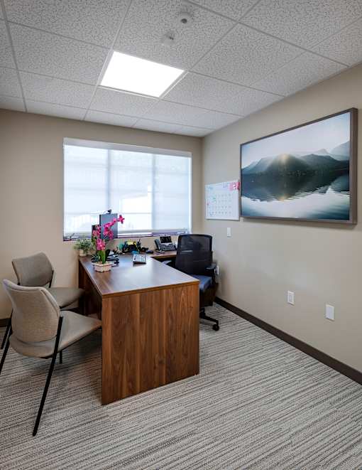 A room with a desk, chair, and a painting on the wall.