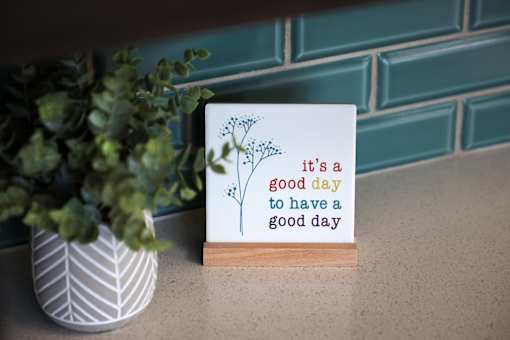 A card with the text "it's a good day to have a good day" is displayed in front of a plant.