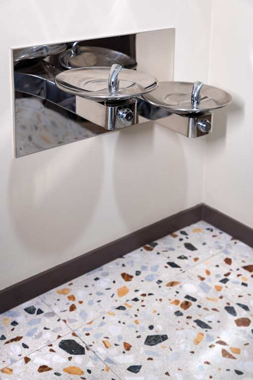 A wall-mounted sink with two bowls is reflected in a mirror.