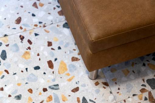 A brown leather chair is placed on a floor with multicolored tiles.