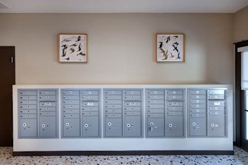 A row of grey lockers are lined up against a wall with two paintings hanging above them.