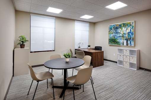 A conference room with a table, chairs, and a painting on the wall.