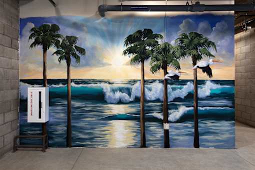 A mural of a sunset with palm trees and surfers.