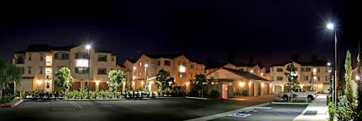 A large building with a parking lot in front of it is lit up at night.