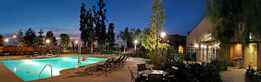 A pool surrounded by trees and chairs at night.