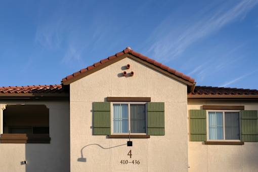 A house with a red tile roof and a window with green shutters.