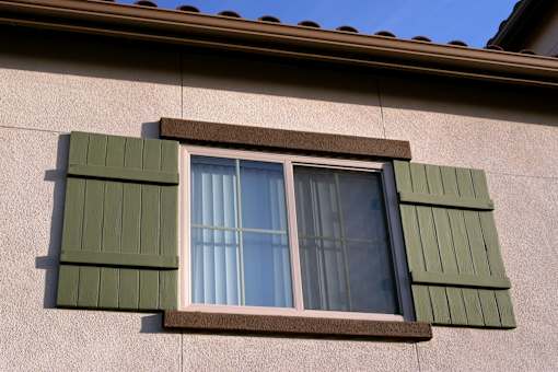 A window with green shutters on a beige wall.